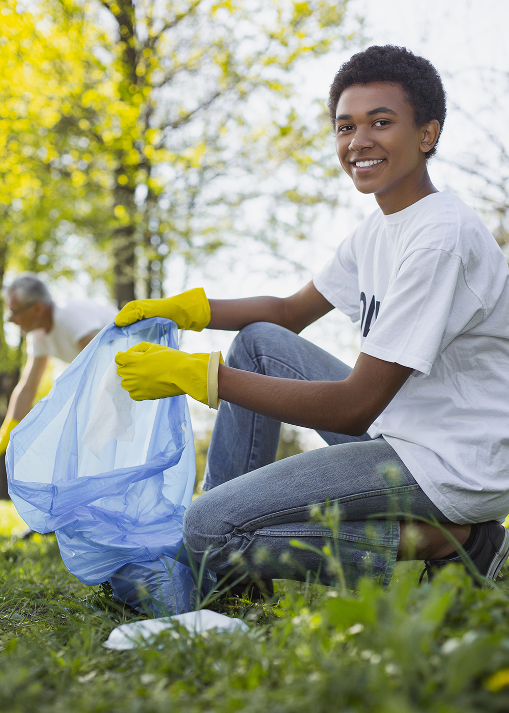 Boy holding a bag wearing white shirt and yellow gloves.