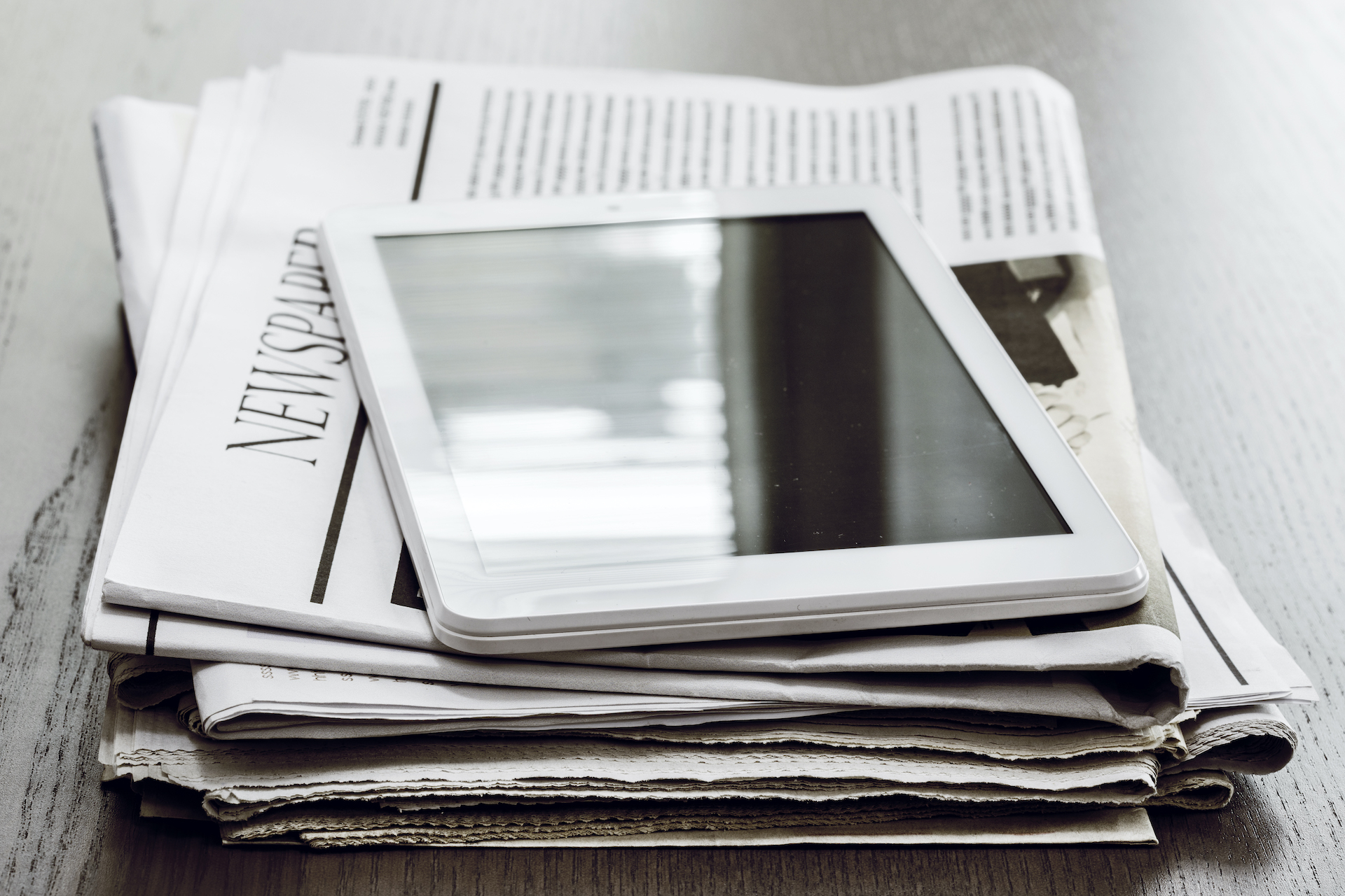 Digital tablet on wooden table with a newspaper to show the distribution of a nonprofit annual report